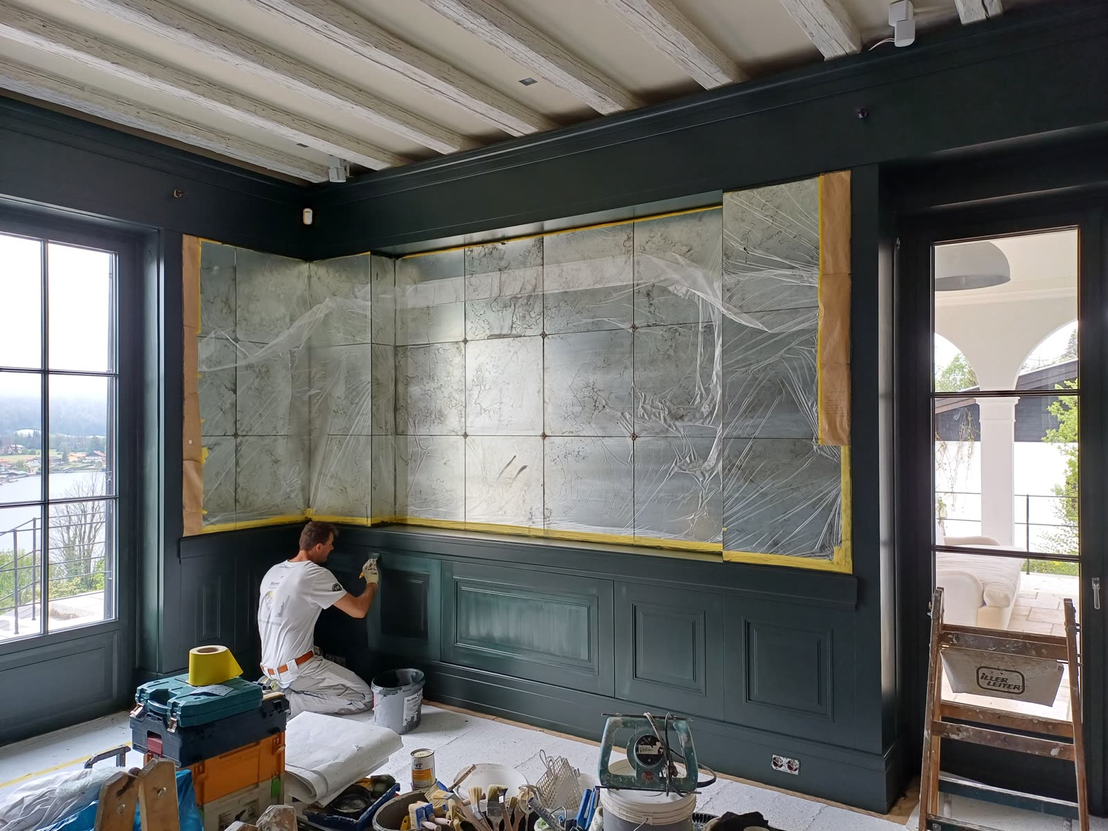 A Hierat painter applies a patina to dark green lacquered wall panelling beneath a mirrored wall