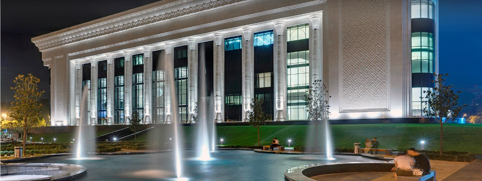 Illuminated facade of a representative building at night with a fountain