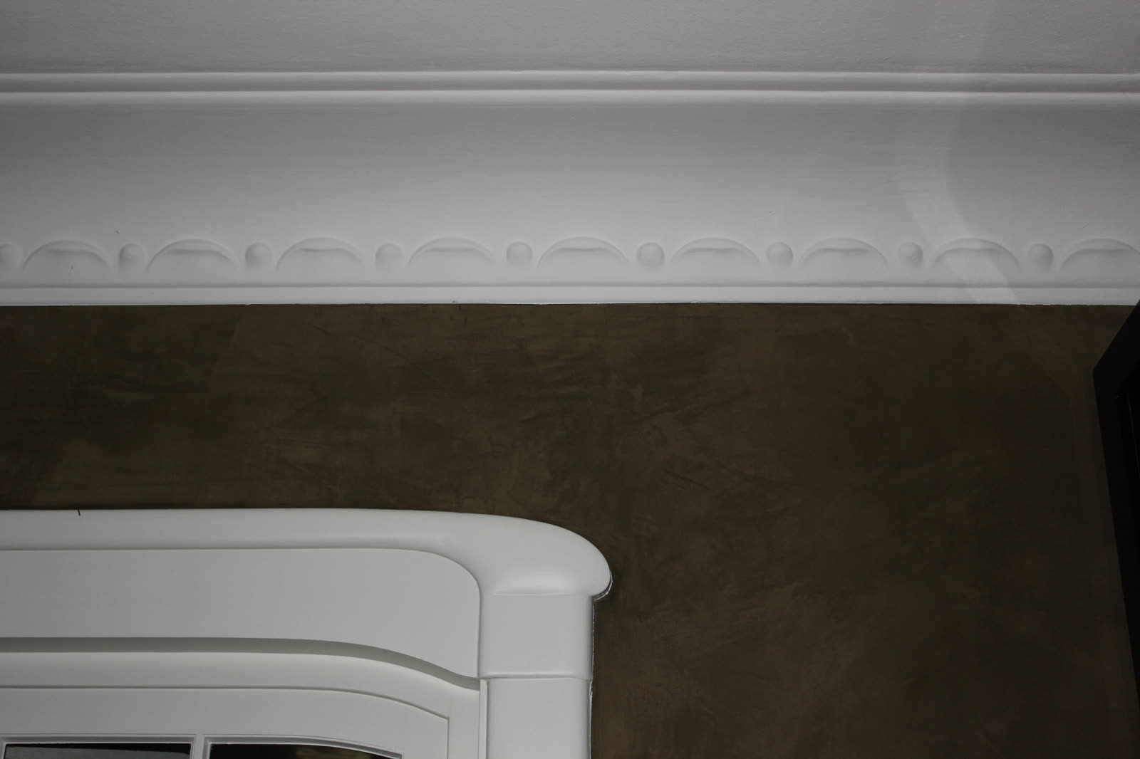 White stucco cornice with ornament above a wall in a trowelled finish