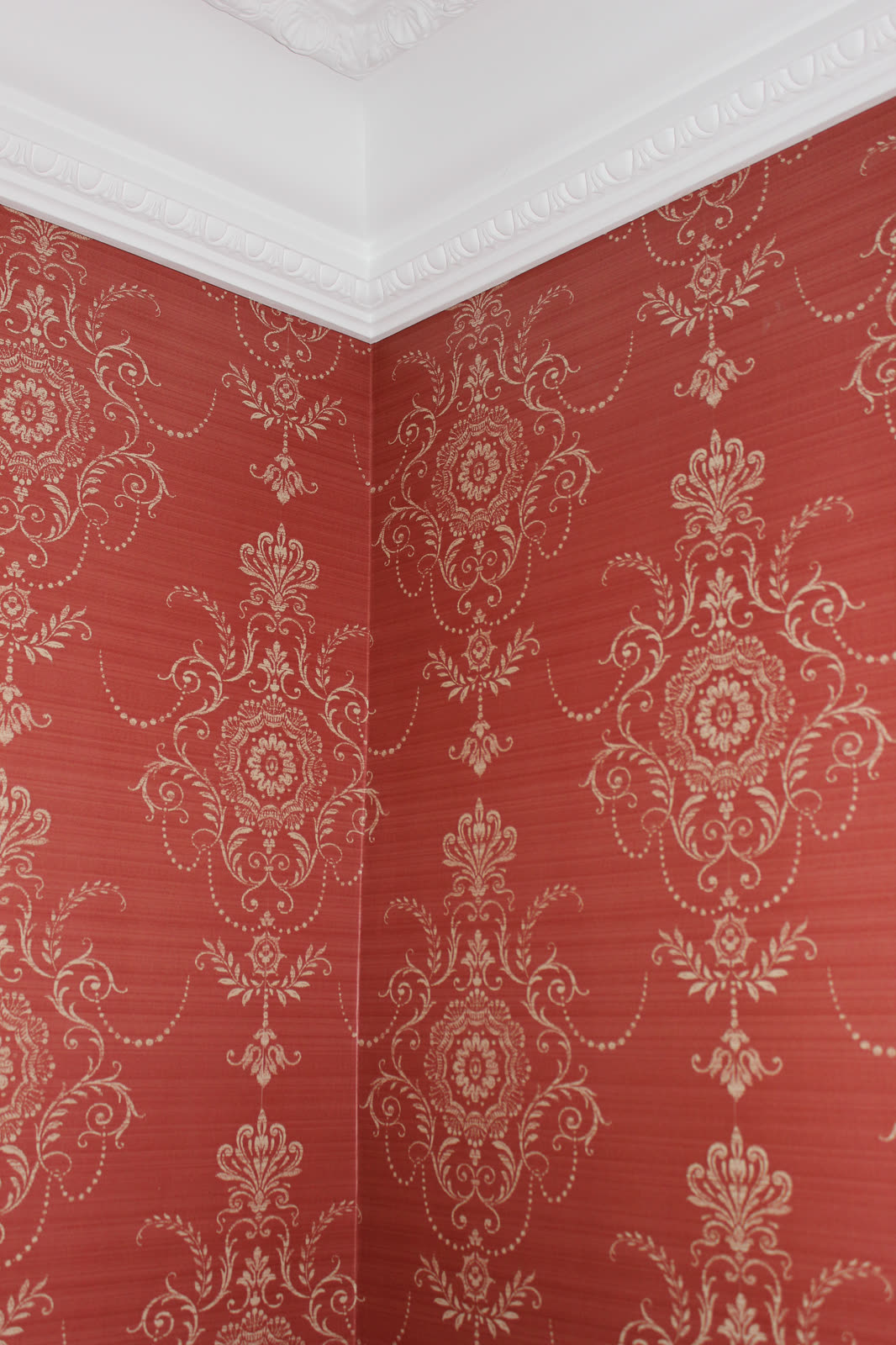 Red ornamental wallpaper with white stucco moulding, hung by Hierat