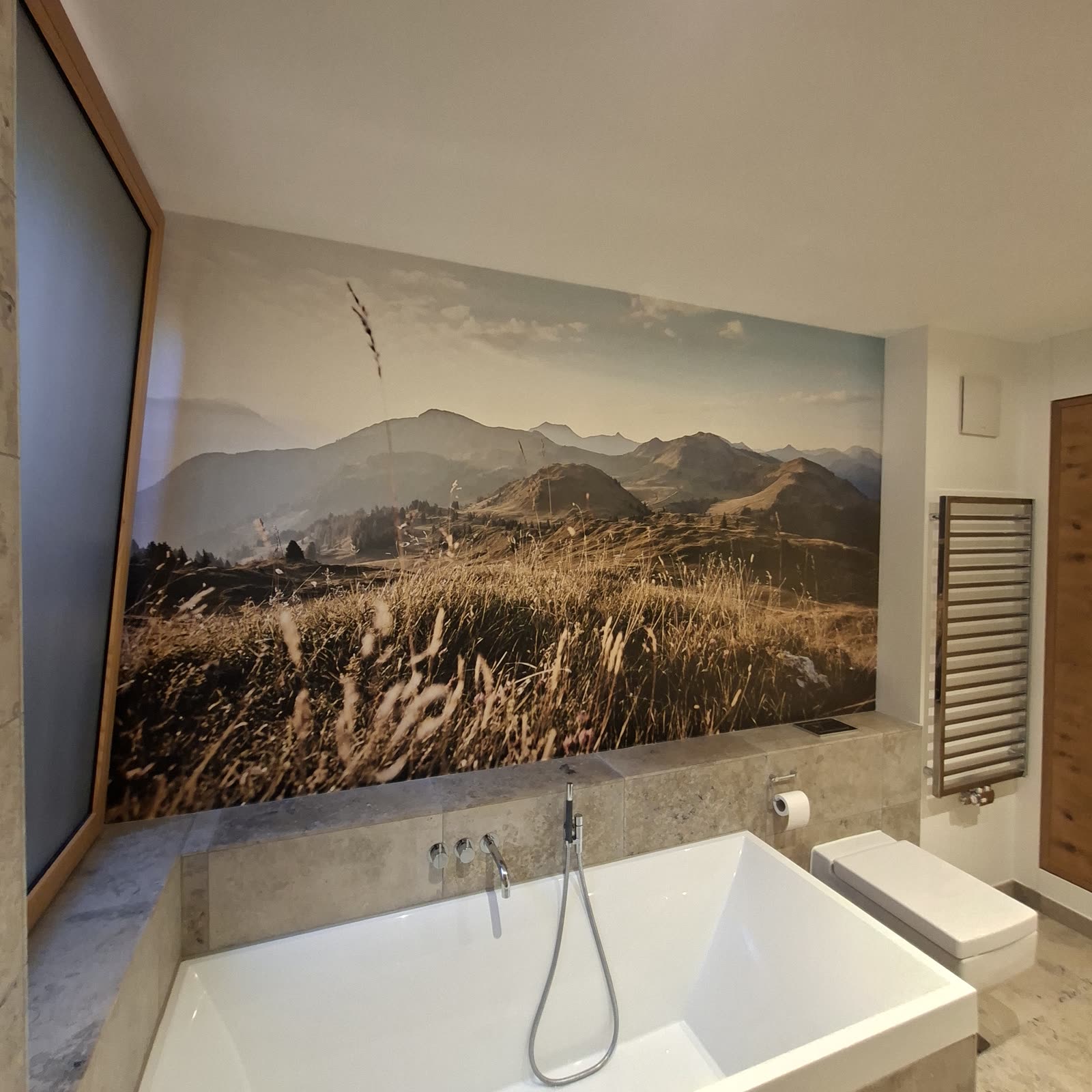 Bathroom with a photo wallpaper of a mountain landscape above the bathtub